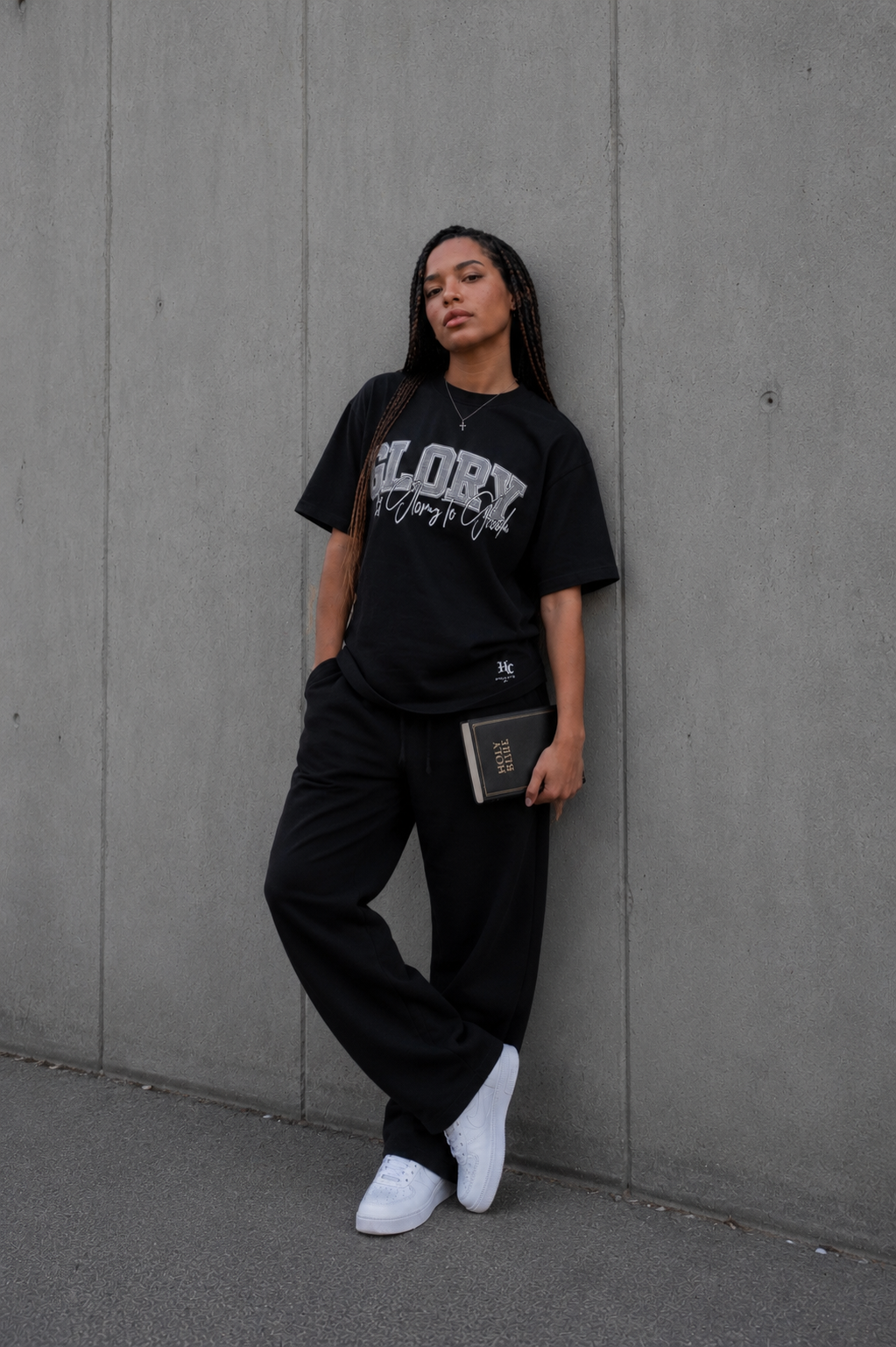 Model trägt das GLORY Oversized T-Shirt von Holyclo in Schwarz und hält eine Bibel in der Hand.
