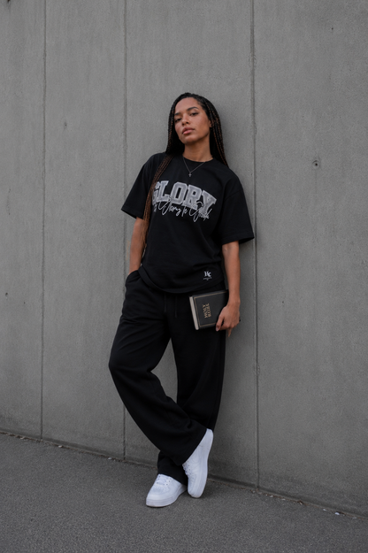 Model trägt das GLORY Oversized T-Shirt von Holyclo in Schwarz und hält eine Bibel in der Hand.